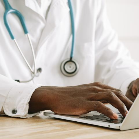 A veterinarian with a stethoscope around his neck sits in front of a laptop